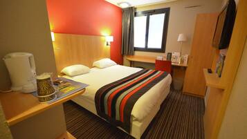 A hotel room with a bed, bedside table, lamp, and a window with curtains.