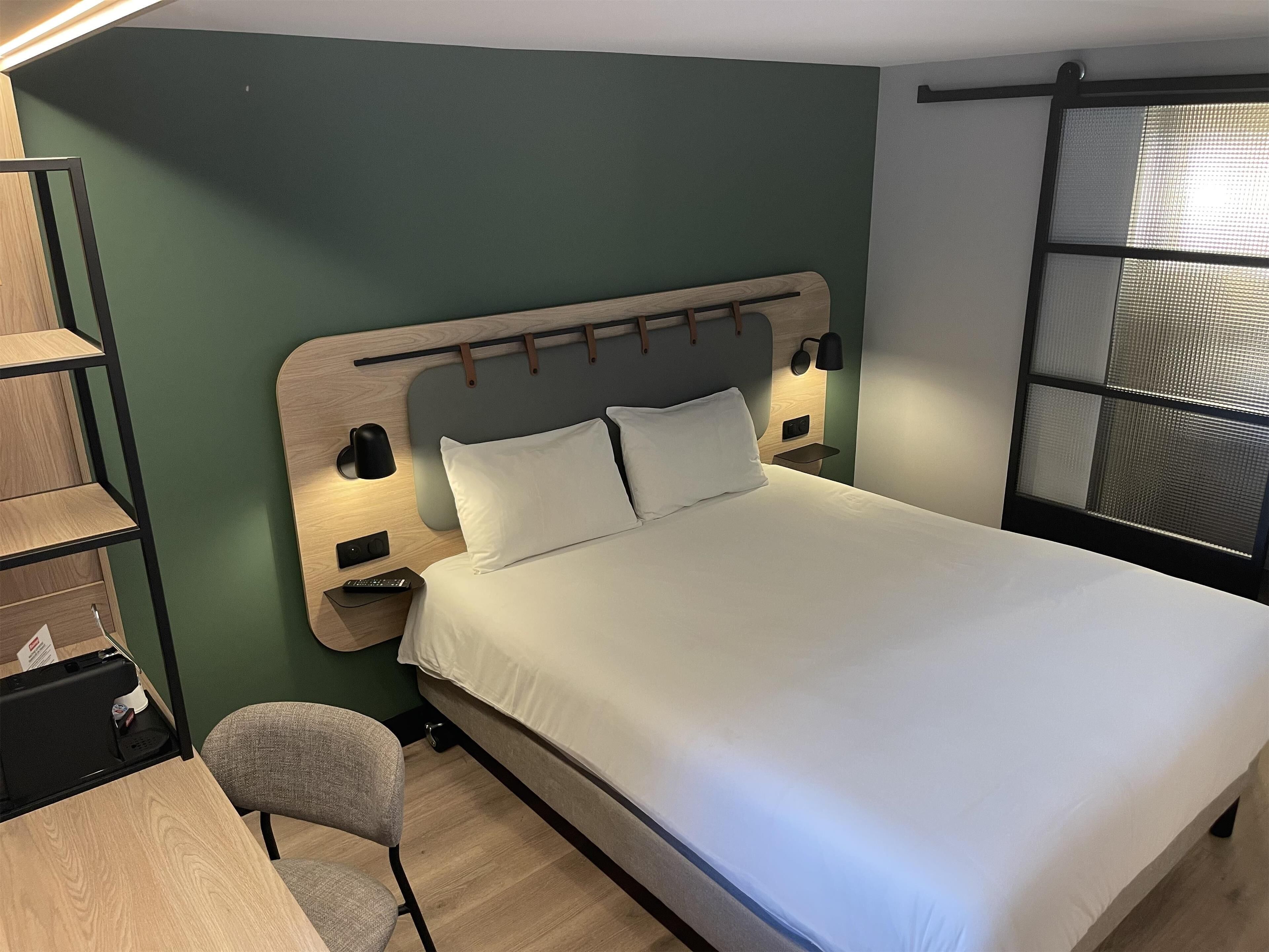 A neatly arranged hotel room with a bed, a desk, and a chair.