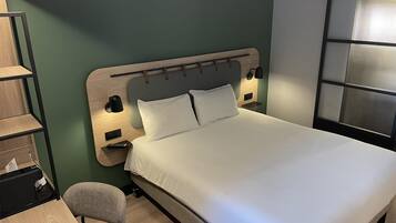 A neatly arranged hotel room with a bed, a desk, and a chair.