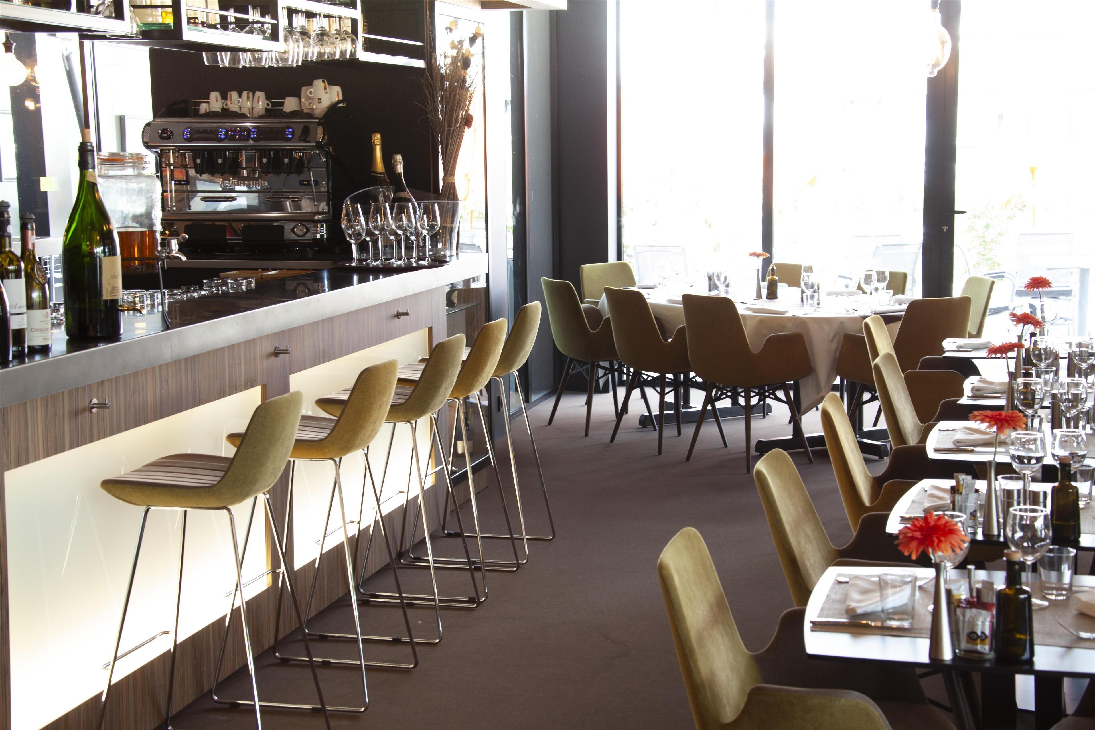 A restaurant with bar seating, tables set for dining, and a bar area with a coffee machine and wine glasses.