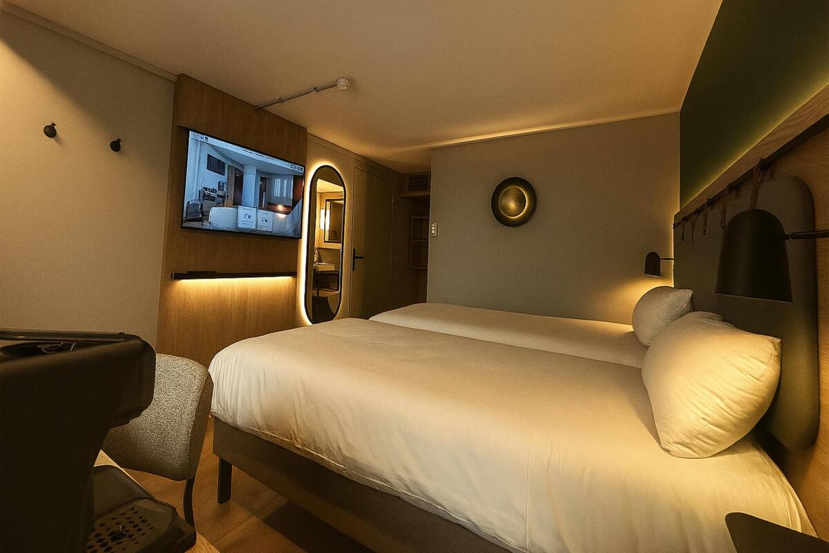 A hotel room with a large bed, a TV mounted on the wall, a mirror, and a small seating area.