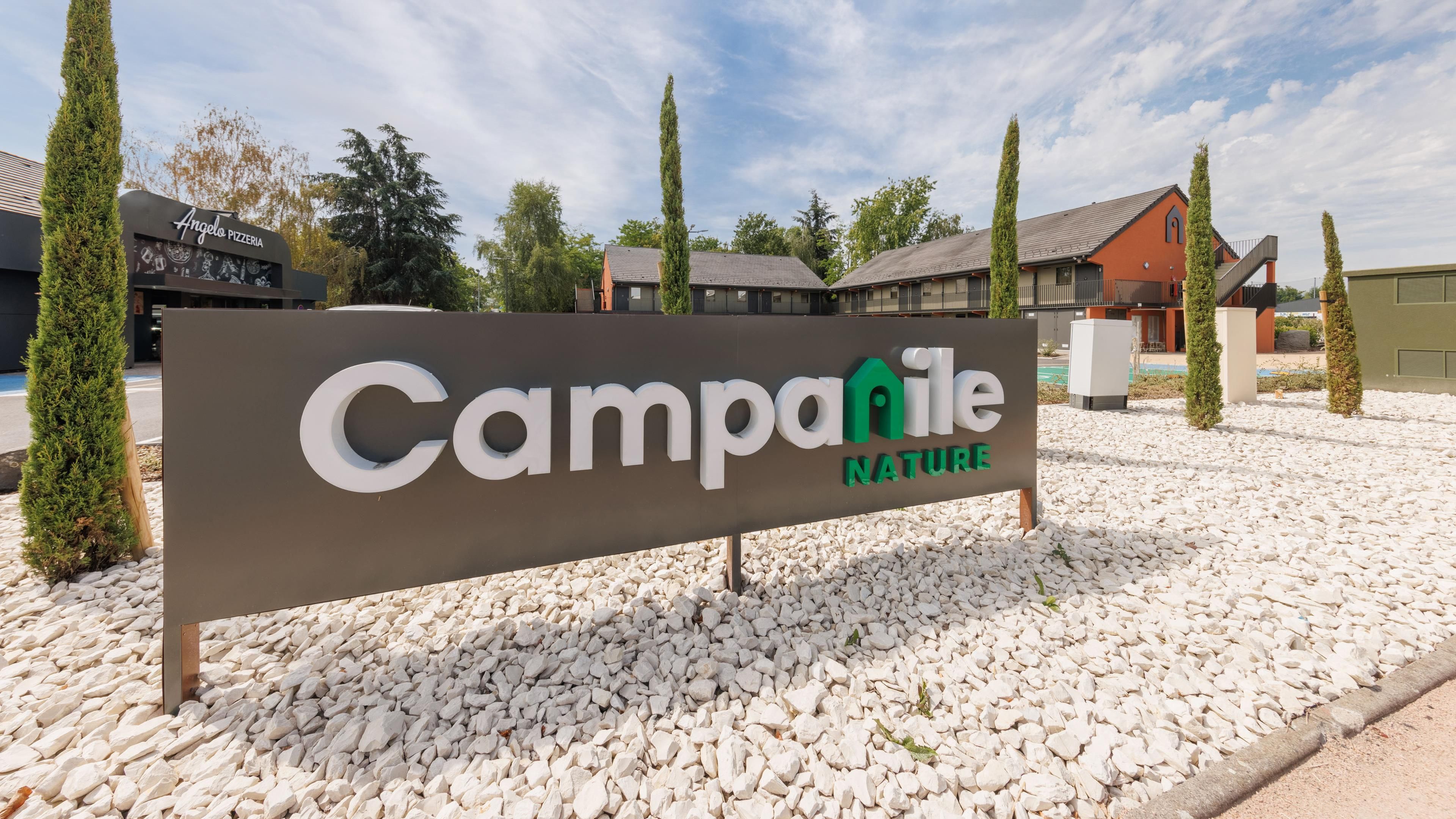 A sign for Campanile Nature with a gravel ground and trees.