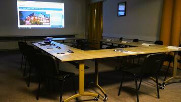 Une salle de conférence avec une longue table, des chaises noires, un ordinateur portable, des documents et un écran de projection affichant une page web.