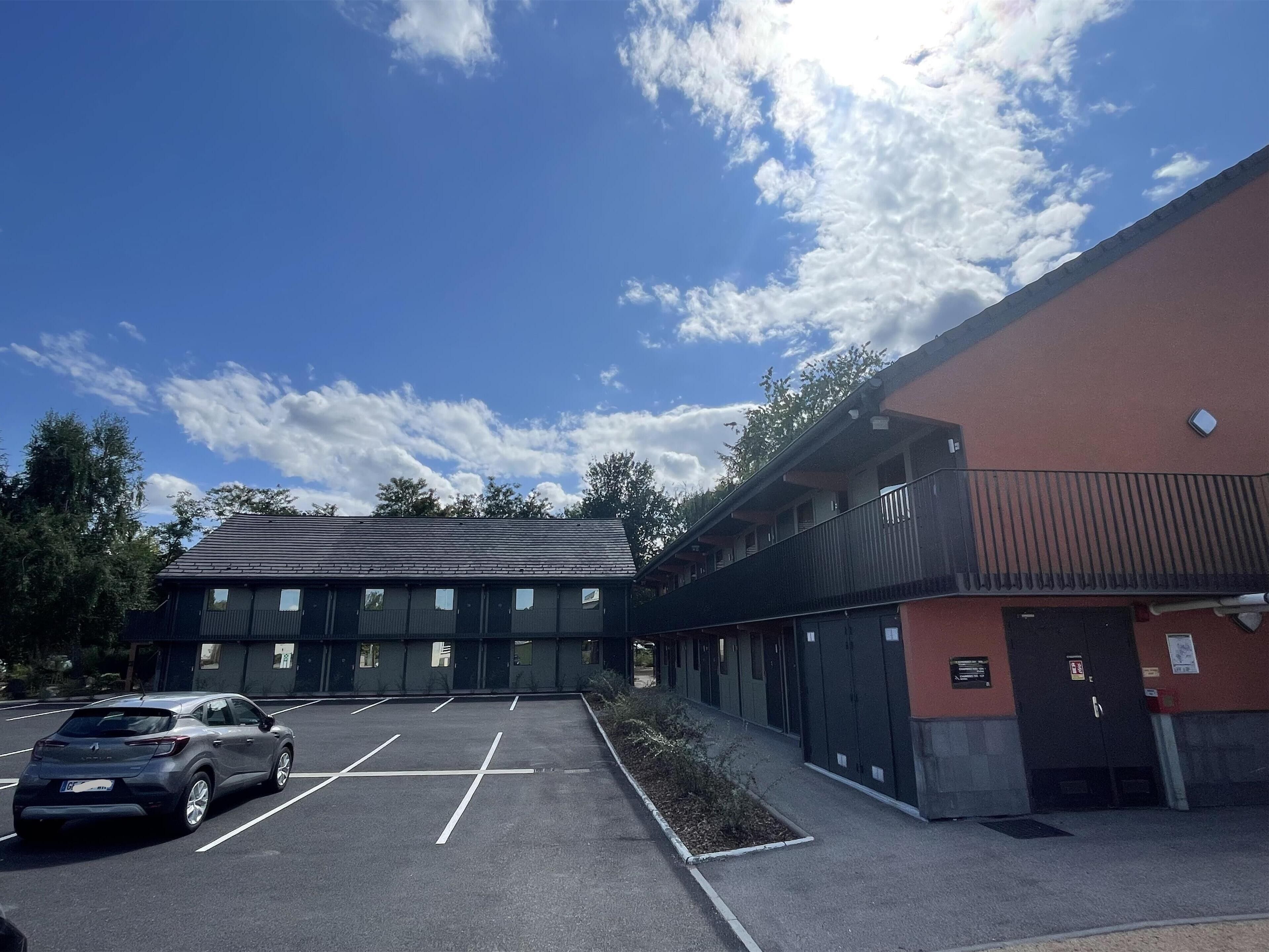 A parking lot with a building that has multiple windows and a balcony.