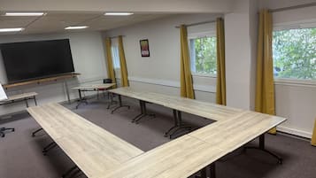 A conference room with a long table, chairs, a blackboard, and windows with curtains.