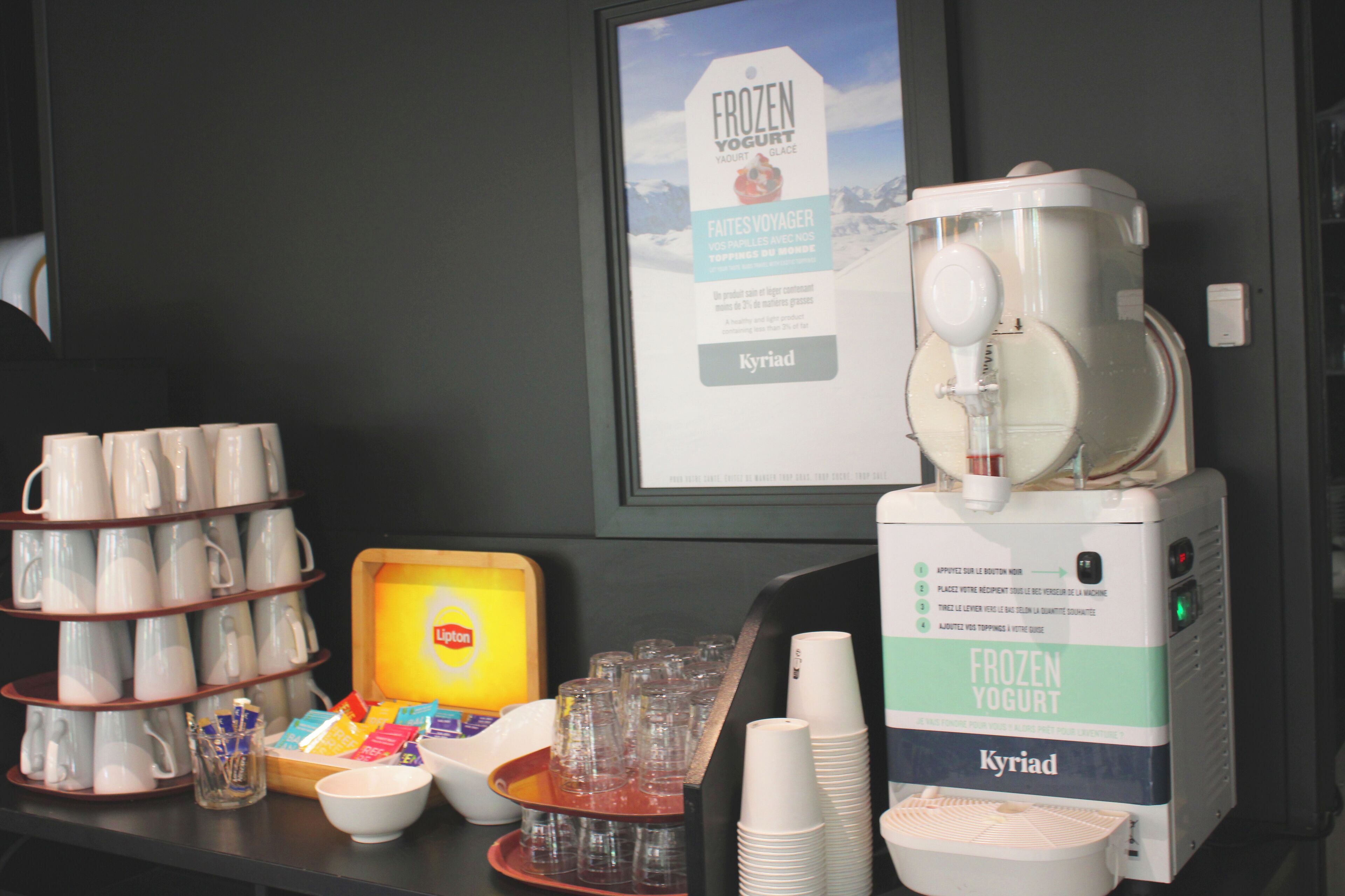 Een ontbijtstation met een bevroren yoghurtmachine, bekers en een schaal met diverse producten.