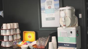 Una estación de desayuno con máquina de yogur helado, vasos y una bandeja de diversos productos.