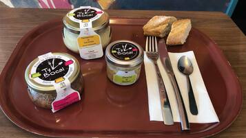 A tray with two jars of Ty Bocal preserves, a small dish of bread, and cutlery on a wooden table.