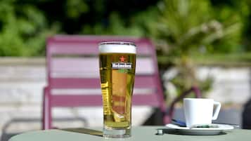 A Heineken glass on a table with a white cup and saucer beside it.