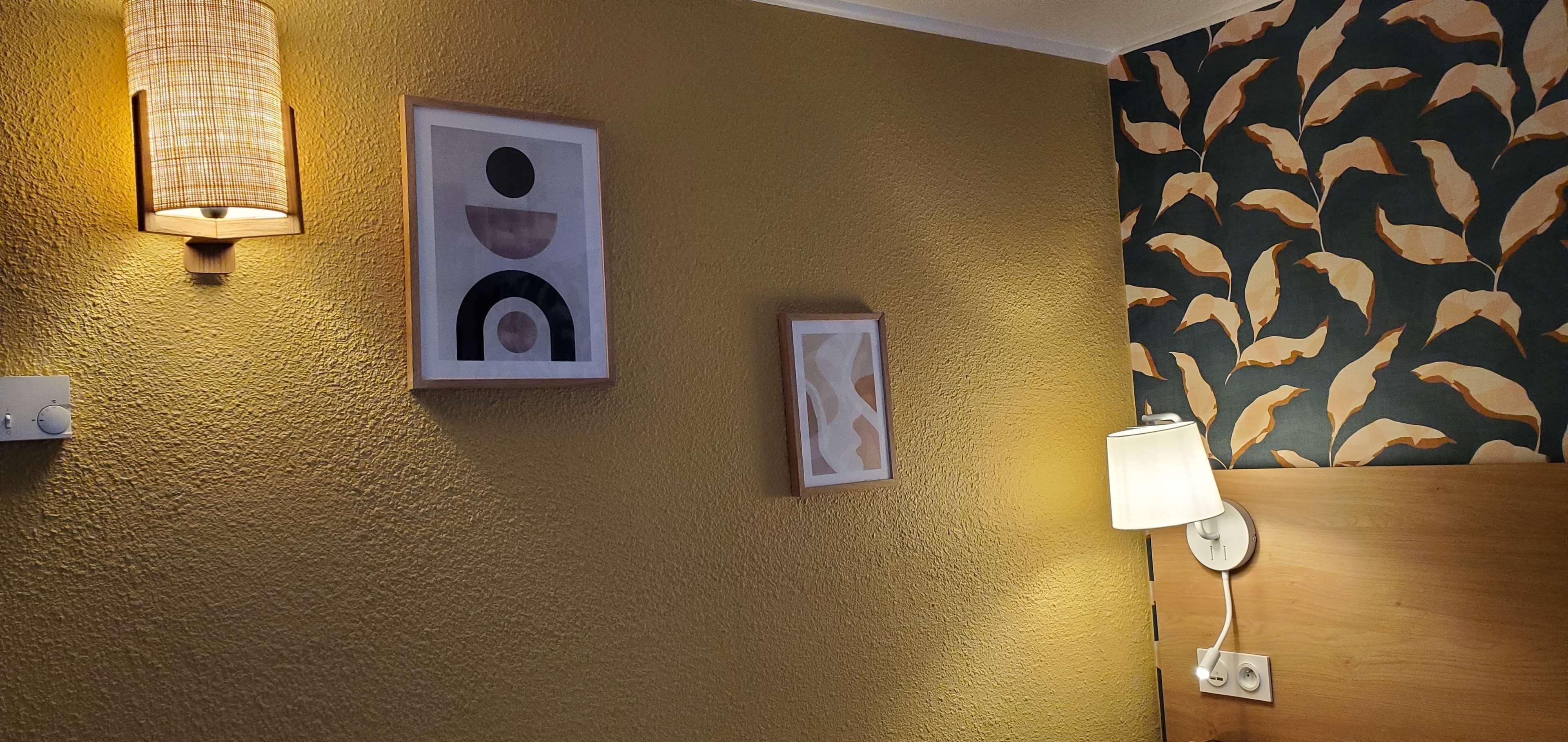 Una habitación con pared de color amarillo texturizado, una obra de arte abstracta enmarcada, un papel tapiz estampado y una lámpara fijada a la pared.