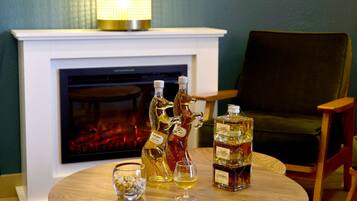 A fireplace with two decorative animal-shaped bottles and a glass of whiskey on a wooden table.