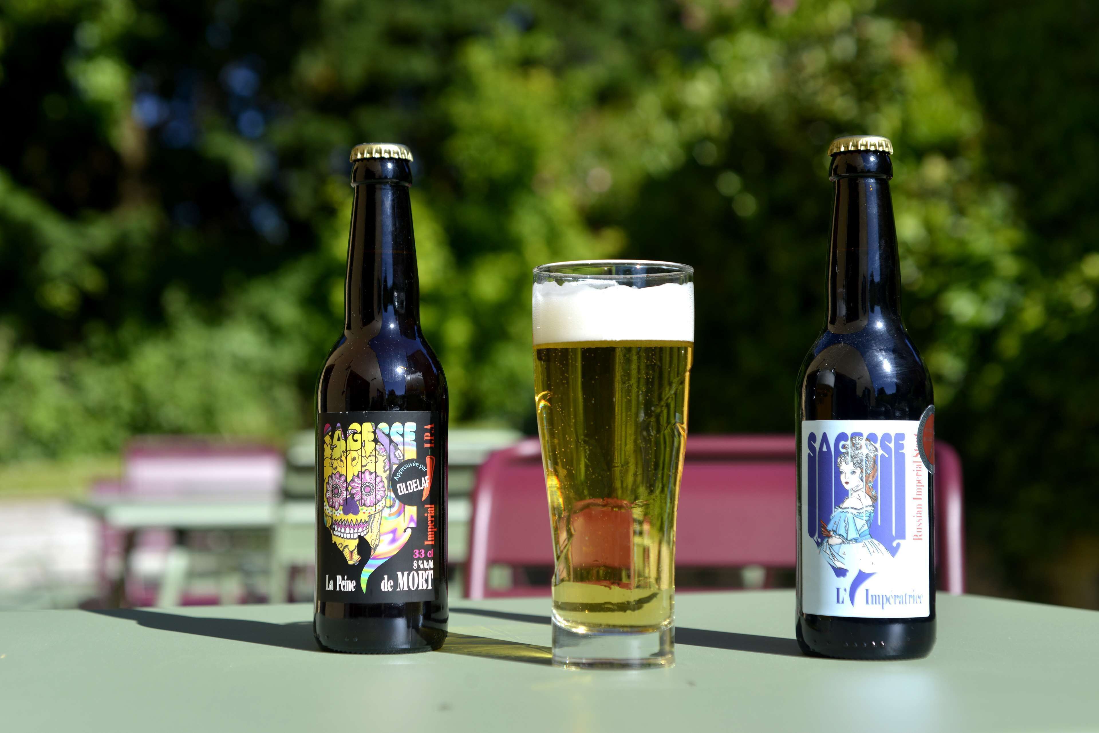 Two bottles of beer and a glass of beer on a table outdoors.