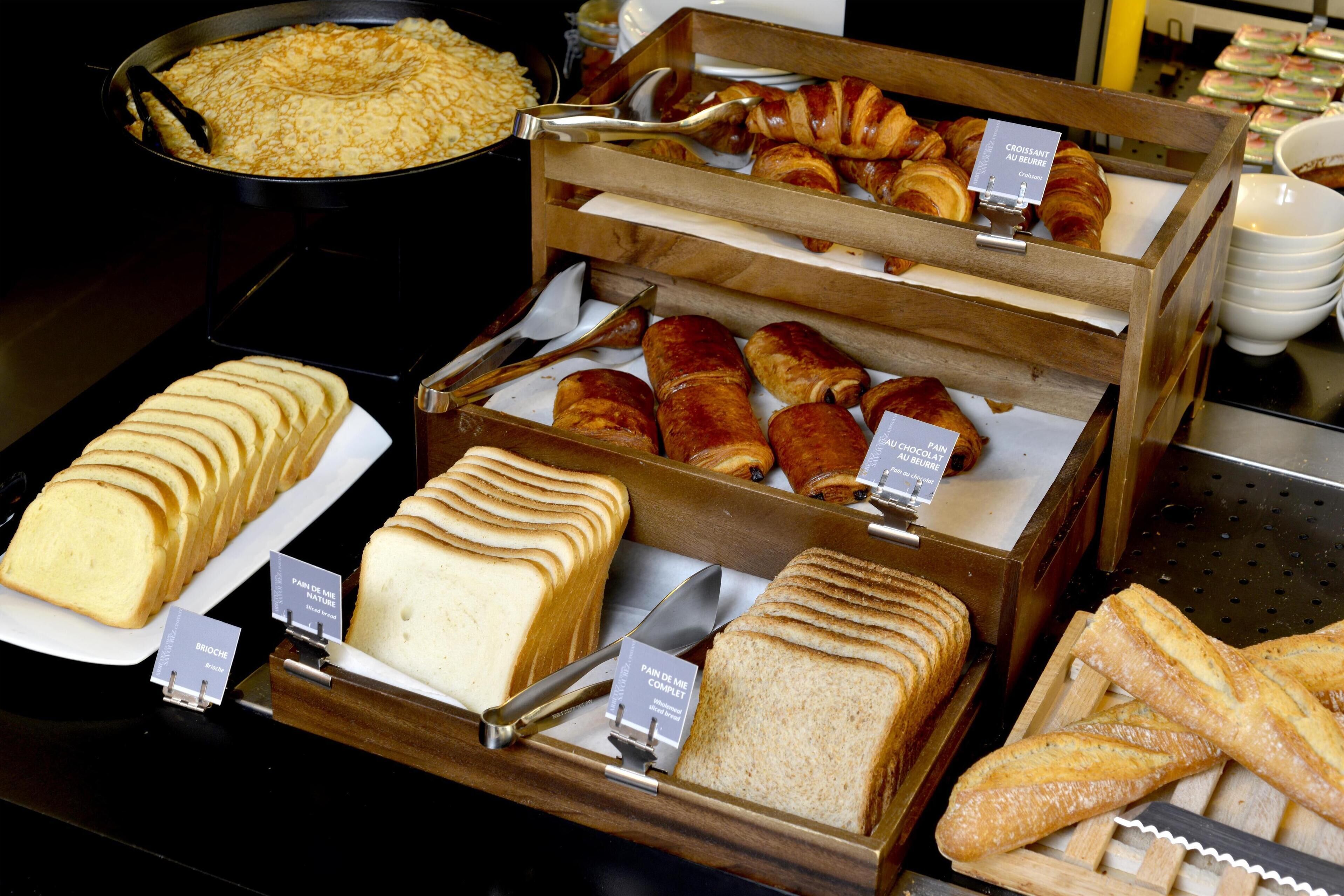 A display of various baked goods including bread, croissants, and pastries in a bakery setting.