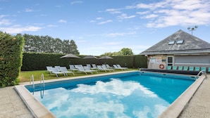 A swimming pool with lounge chairs and umbrellas, a lifebuoy, and a building with a garage door. - Kyriad - Deauville St Arnoult (Saint-Arnoult)