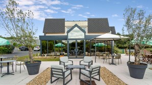 An outdoor patio area with tables and chairs, surrounded by potted plants and umbrellas. - Kyriad - Deauville St Arnoult (Saint-Arnoult)