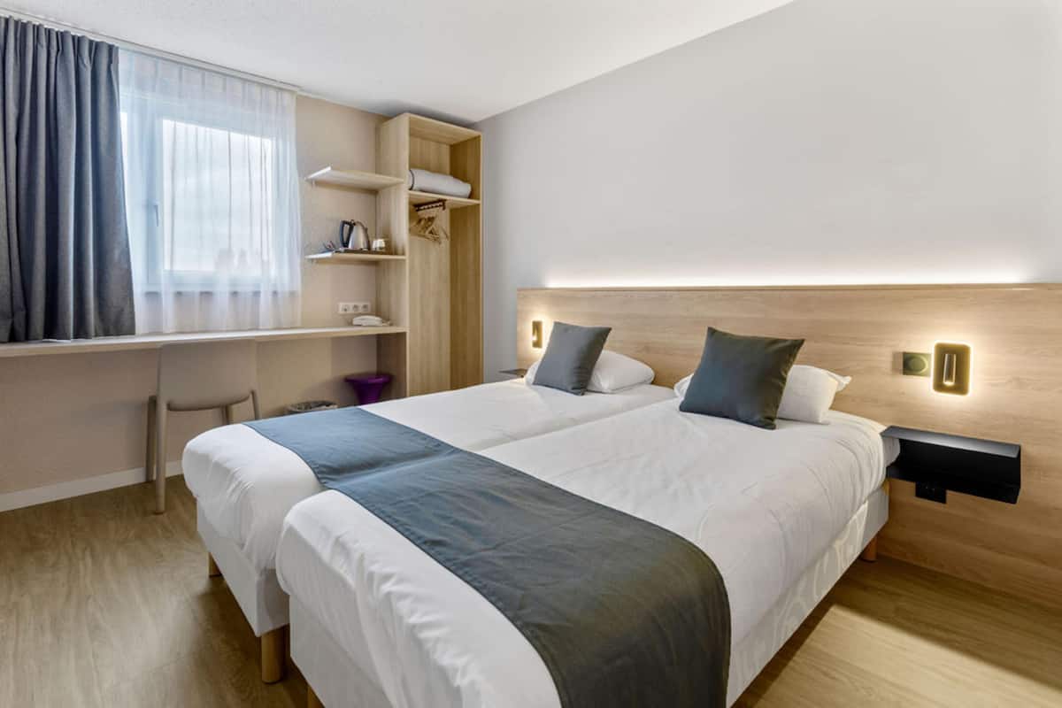 A modern hotel room with two beds, a desk, and a built-in wardrobe.