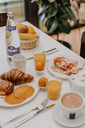 A breakfast table with croissants, eggs, orange juice, and a bottle of Thonon water. - Kyriad - Deauville St Arnoult (Saint-Arnoult)