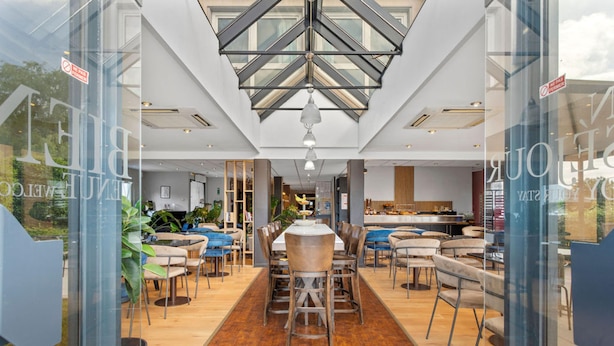 A modern dining area with a high ceiling, glass walls, and a central table with chairs. - Kyriad - Deauville St Arnoult (Saint-Arnoult)
