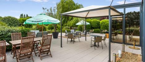 An outdoor patio area with wooden tables and chairs, covered by a large canopy.