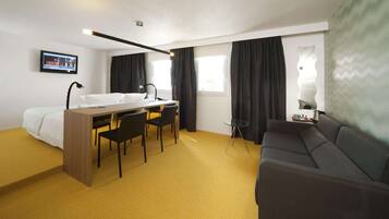 Une chambre d’hôtel comprenant un lit, un bureau avec une chaise, un canapé, une télévision et une fenêtre avec des rideaux.