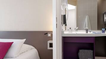 A hotel room with a bed, a bathroom with a mirror, a sink, and a towel rack.