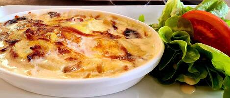Un bol blanco con gratin sobre un plato, acompañado de una ensalada.