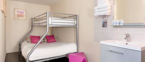 A bunk bed with pink pillows, a small pink stool, a white sink, and a mirror with towels.