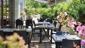 Un área de comedor al aire libre con mesas y sillas, rodeada de follaje y flores.