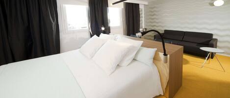 Una habitación de hotel moderna con una cama grande, una mesita de noche de madera, una pequeña mesa redonda, un sofá y una pared con un estampado ondulado.