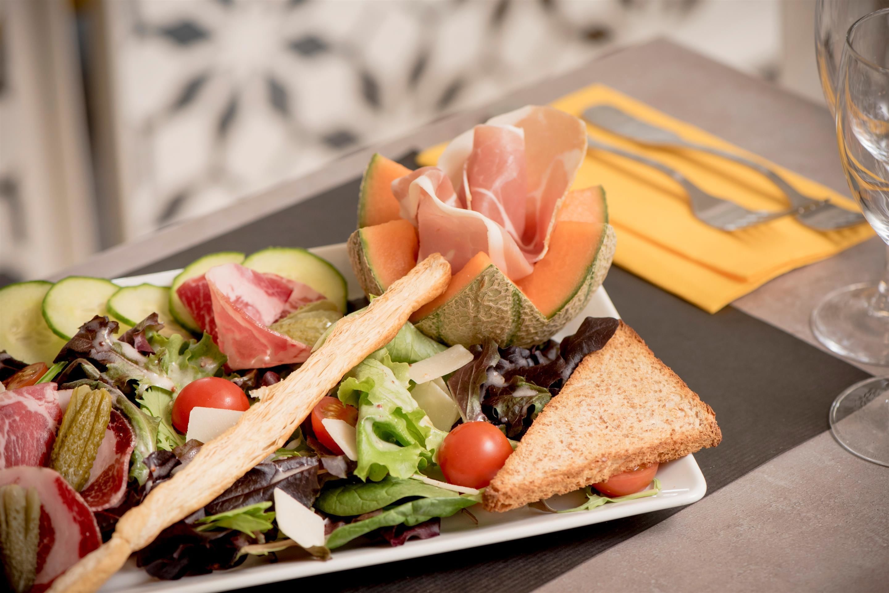 A plate of food with a salad, melon, and prosciutto.