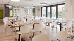 Un comedor moderno con sillas y mesas blancas, paneles decorativos y ventanas grandes.
