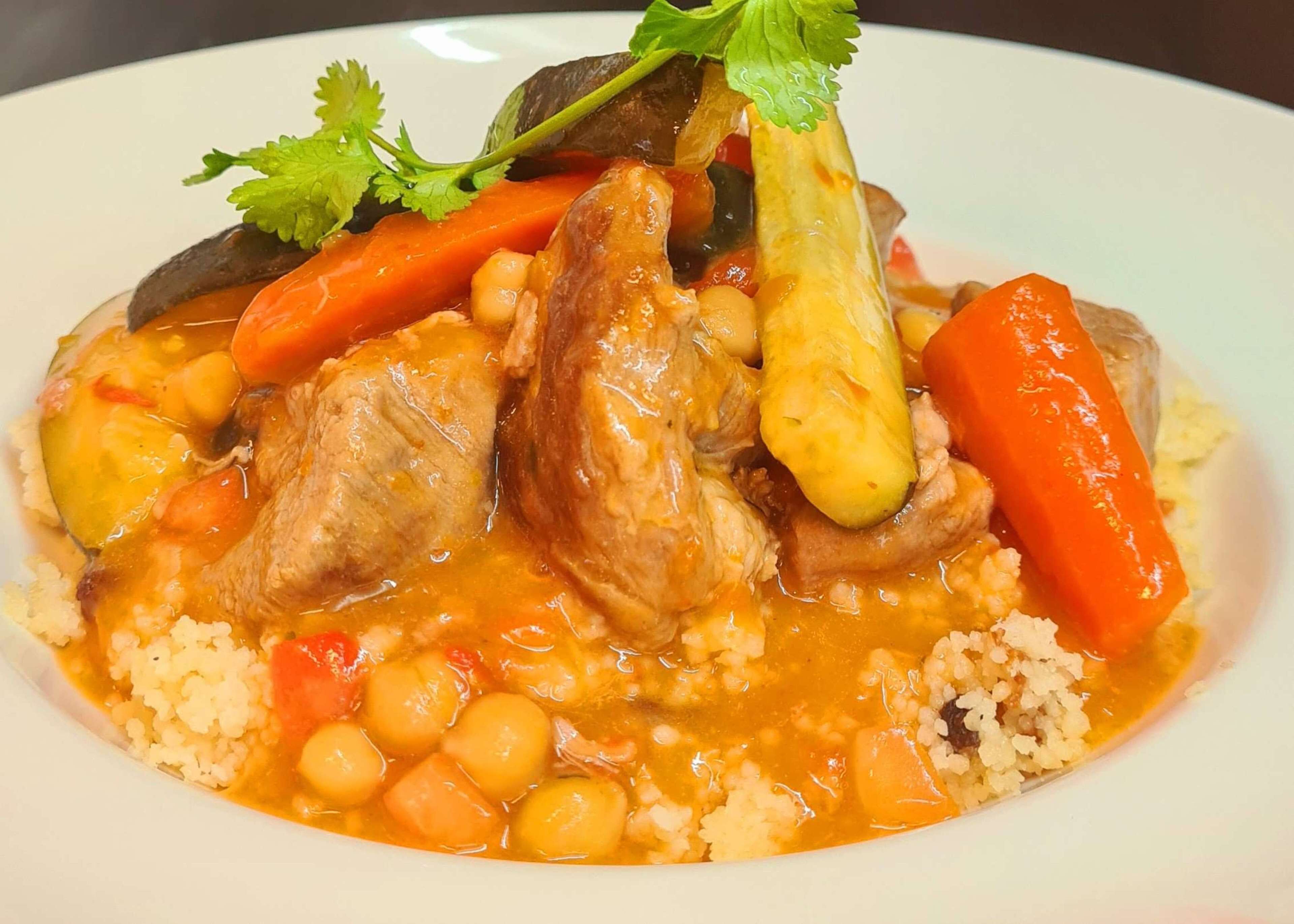 Een bord met kippenragout, groenten en couscous.