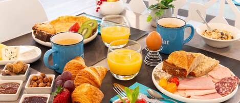 Una mesa de desayuno con croissants, fruta, huevos y jugo.