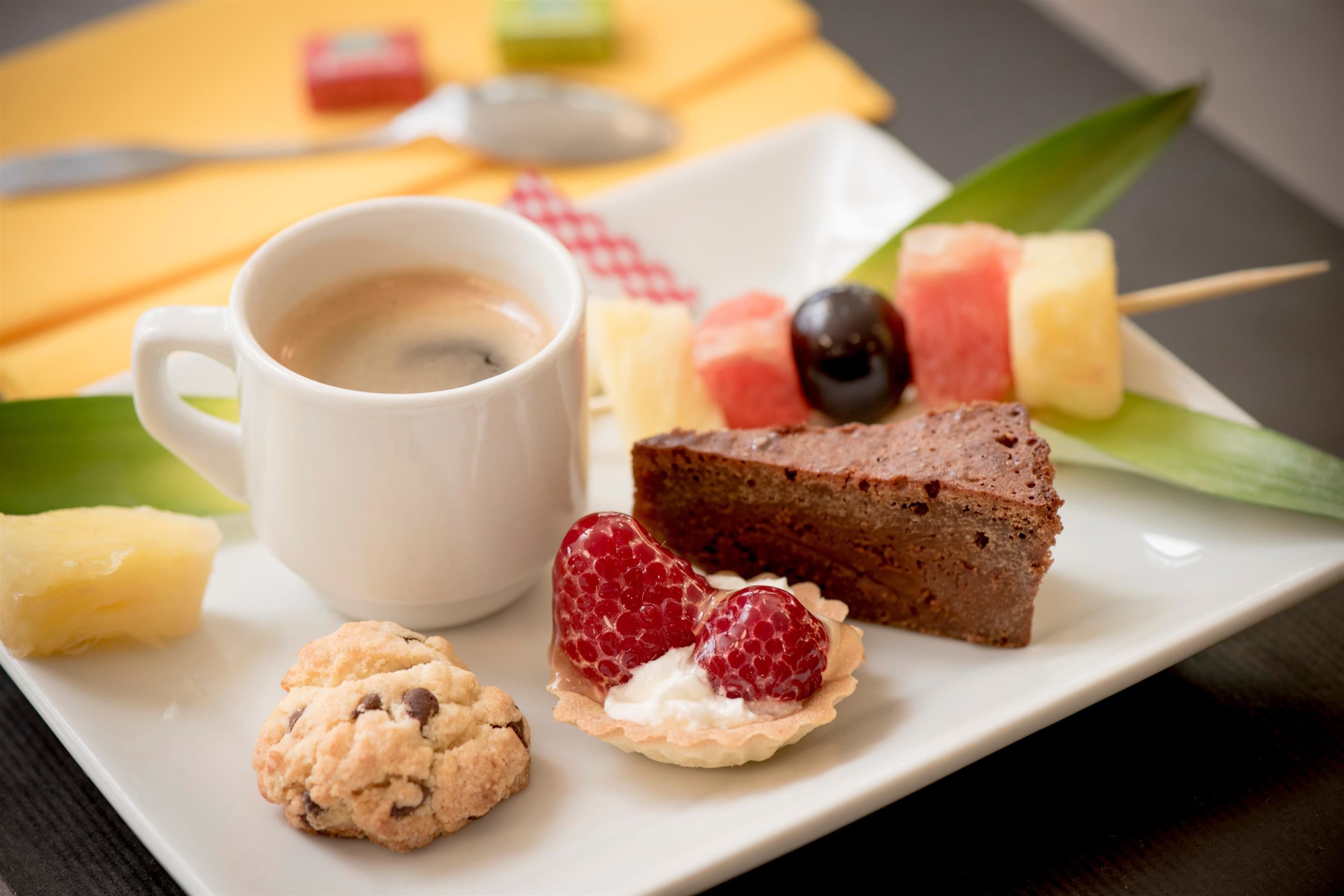 A dessert plate with a slice of cake, strawberries, a cookie, and a cup of coffee.