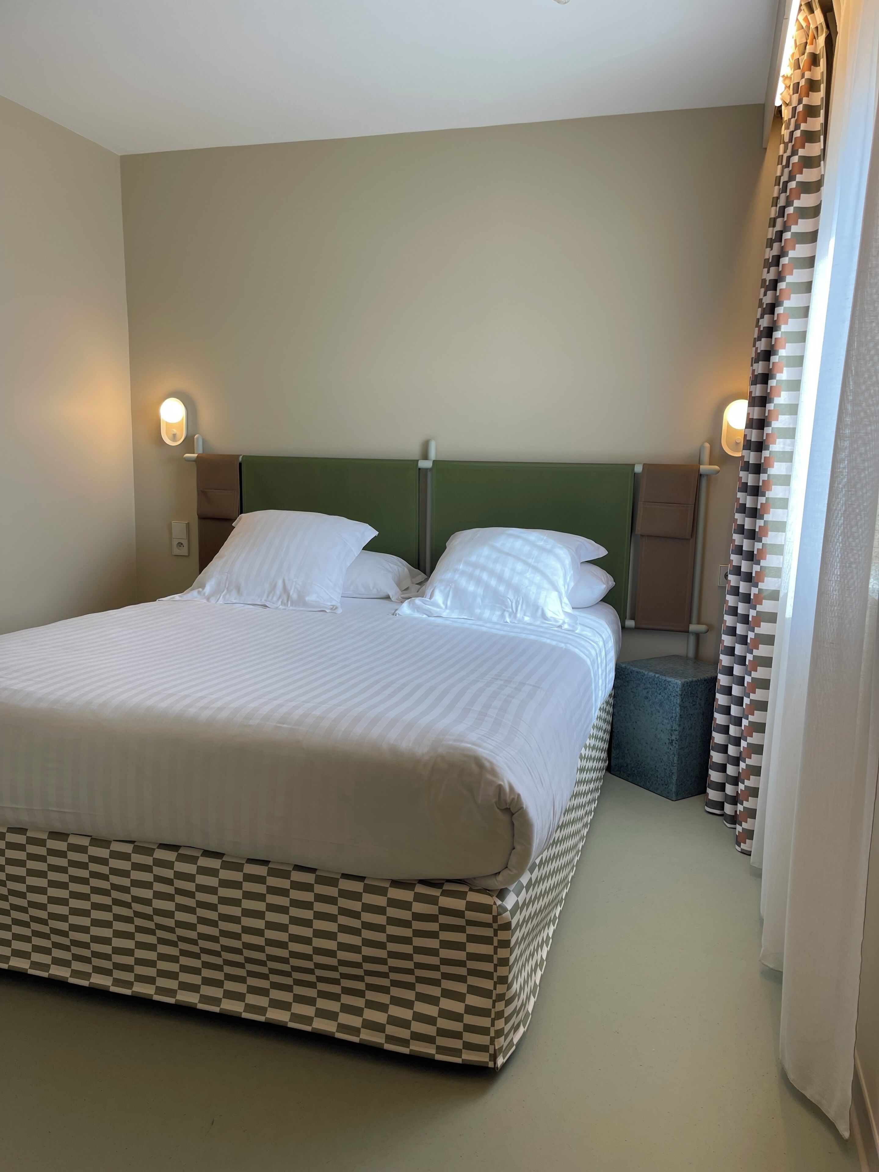 A neatly made bed with white linens, a green headboard, and two bedside lamps.
