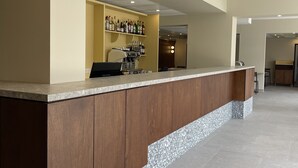 A modern bar area with a counter, shelves of liquor bottles, and a seating area in the background. - Hotel des Victoires by Soniho (Cannes)