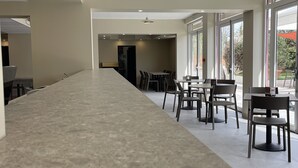 A spacious, modern hotel lobby with a long, polished concrete floor, a high ceiling with a central light fixture, and large windows offering views of the outdoors. - Hotel des Victoires by Soniho (Cannes)