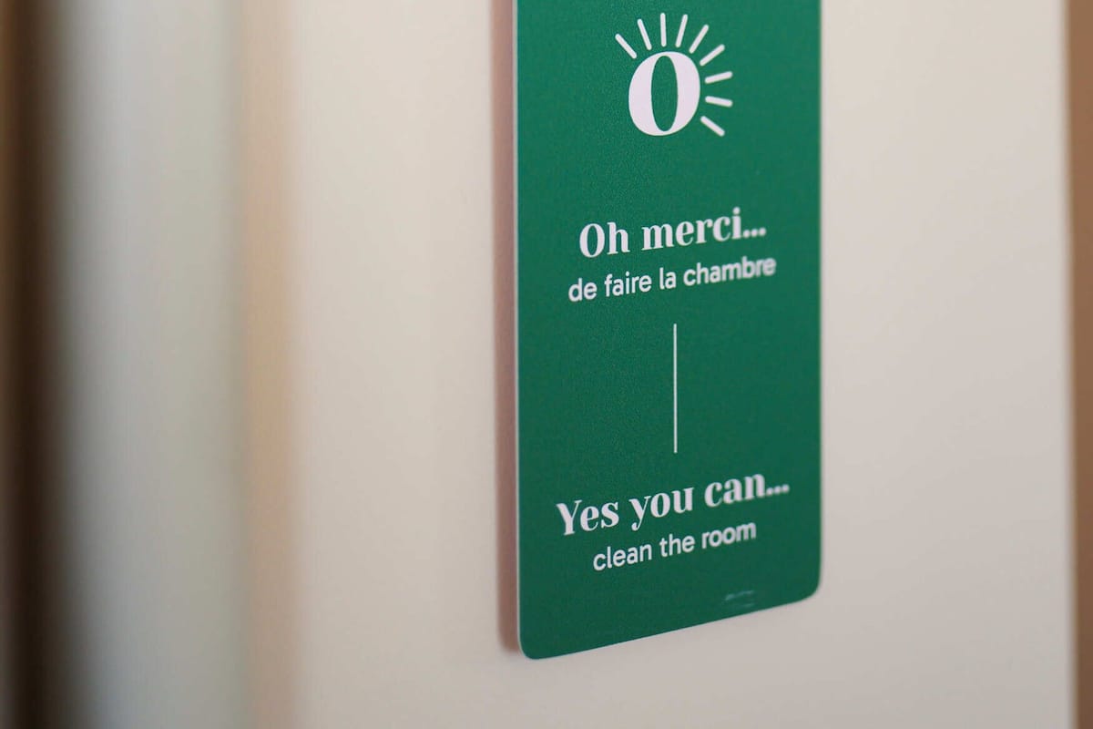 Uma etiqueta verde com texto em francês e inglês, presa a uma parede perto de um cano branco.