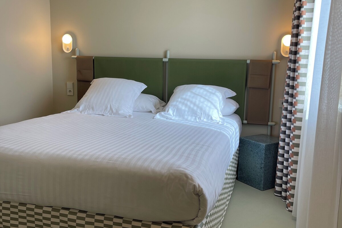 A neatly made bed with white linens, a green headboard, and two bedside lamps.