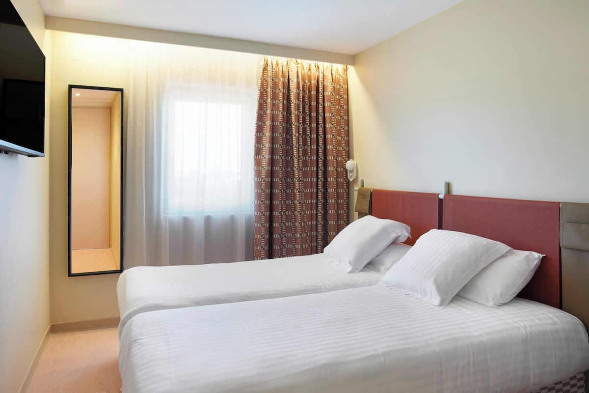 Quarto de hotel com uma cama, televisão presa à parede e janela com cortinas.