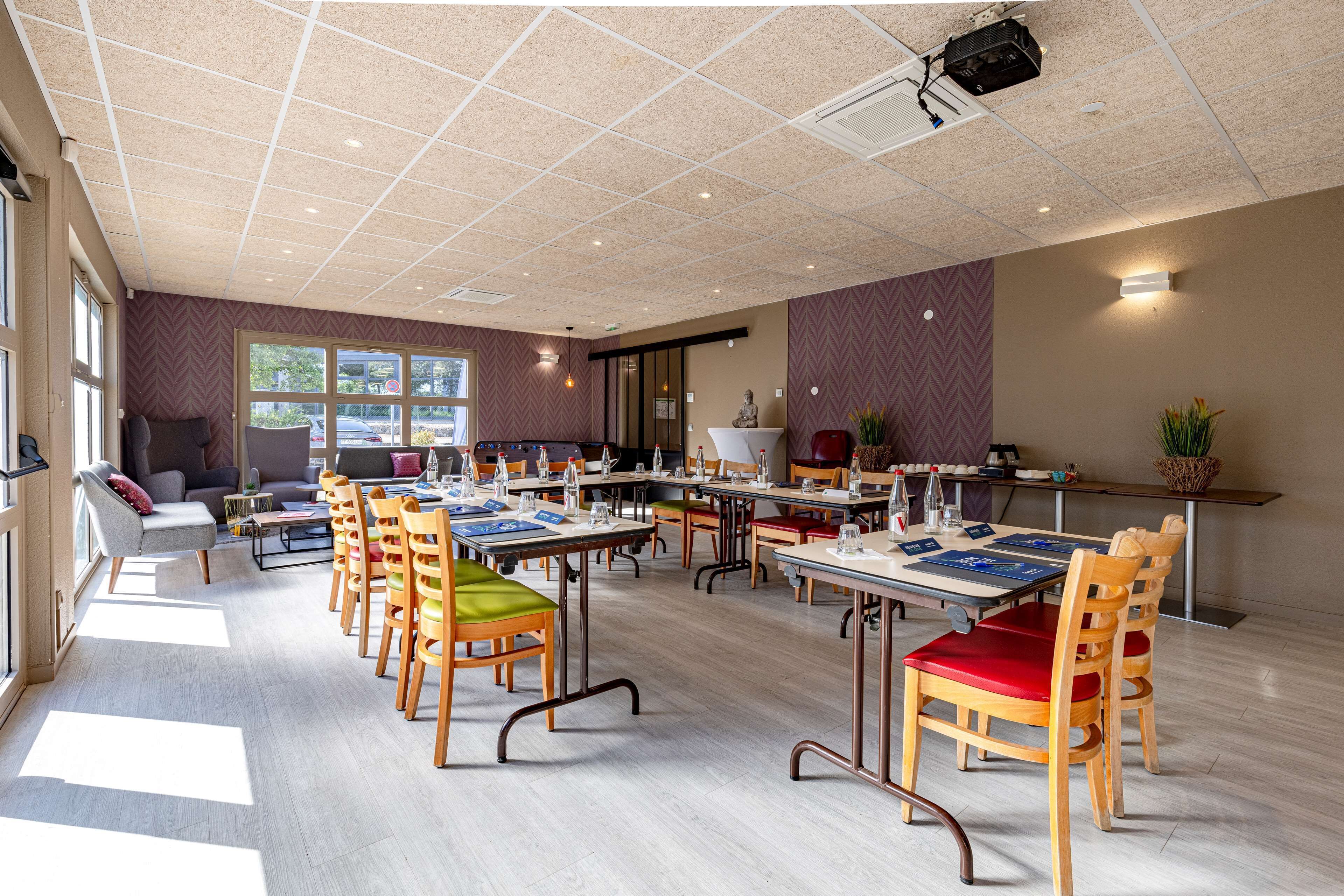A spacious room with multiple tables and chairs, large windows, and a modern ceiling design.