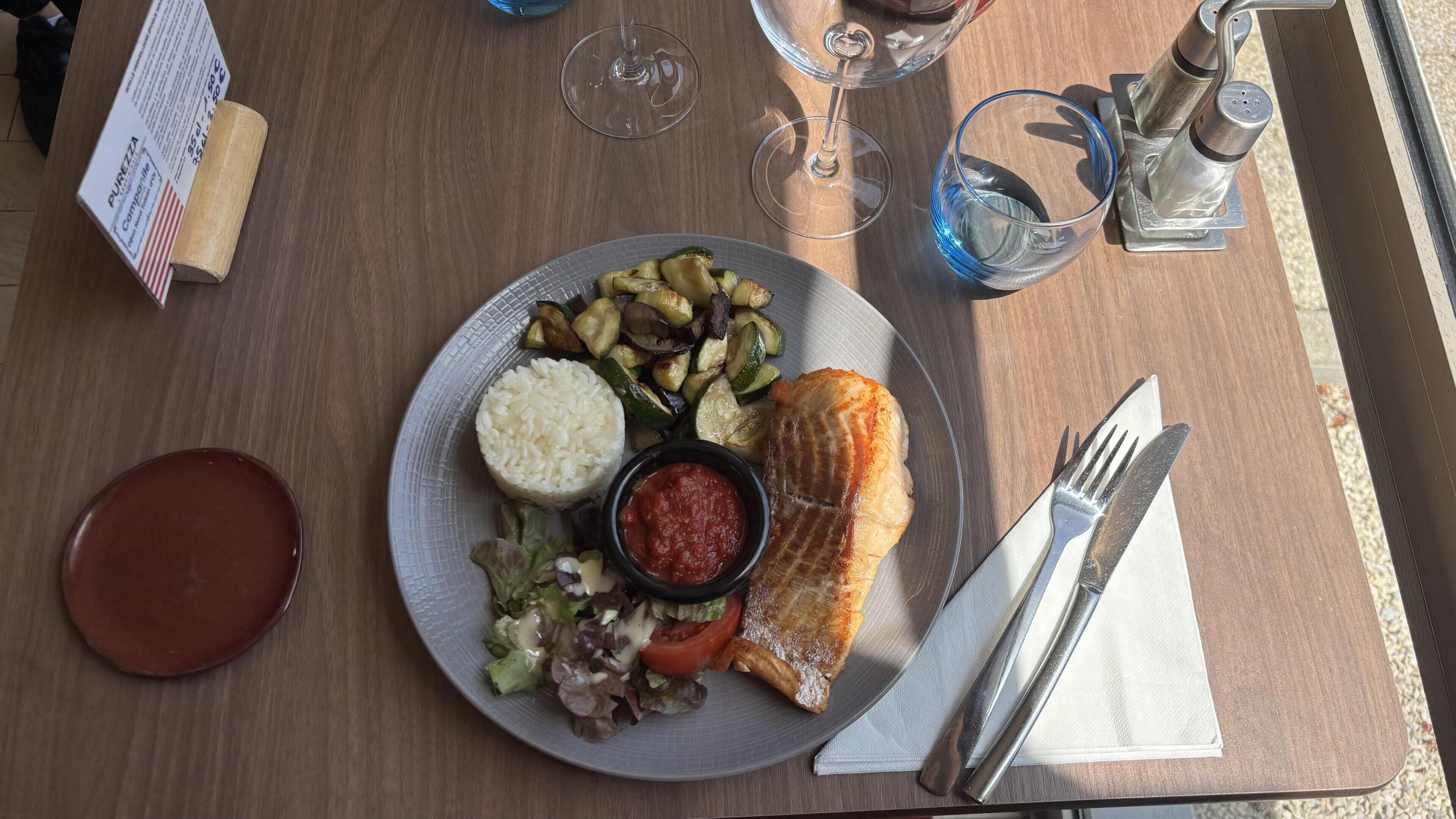 Una mesa con un plato de comida, un vaso de agua, una copa de vino y un salero.
