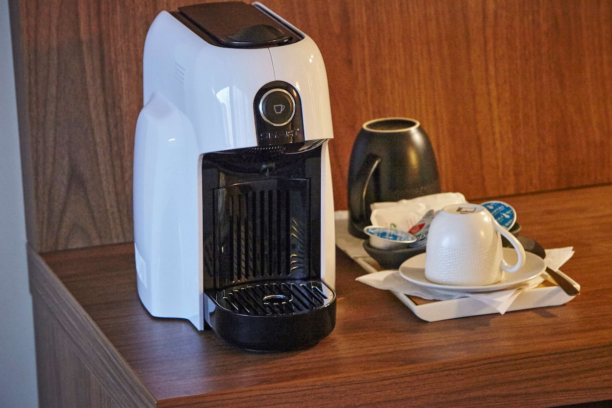 Una cafetera sobre una mesa de madera, con una taza y platillo, una jarra y un cuenco pequeño.