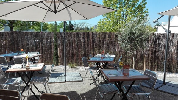 An outdoor patio area with tables and chairs, umbrellas, and a decorative fence.