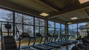 Un gimnasio con cintas de correr y bicicletas estáticas, ventanas amplias y suelo de hormigón.