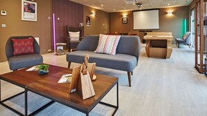 Una sala moderna con un sofá gris, una mesa de centro de madera y una planta pequeña. Se observa una pantalla de proyector y un mueble de madera al fondo.