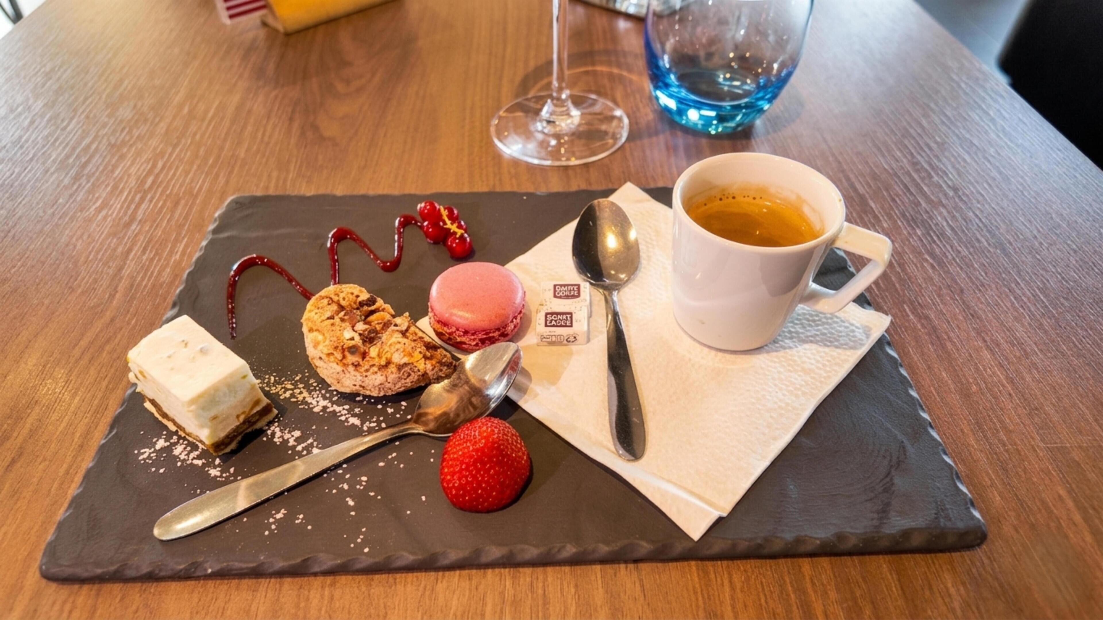 Bandeja de postres con macarons, una fresa y una bola de helado sobre una tabla de pizarra, acompañada de una taza de café y una cuchara.