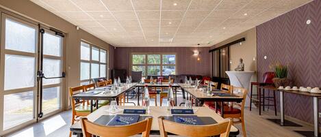 Un'ampia sala da pranzo con diversi tavoli e sedie, ampie finestre e un moderno design del soffitto.