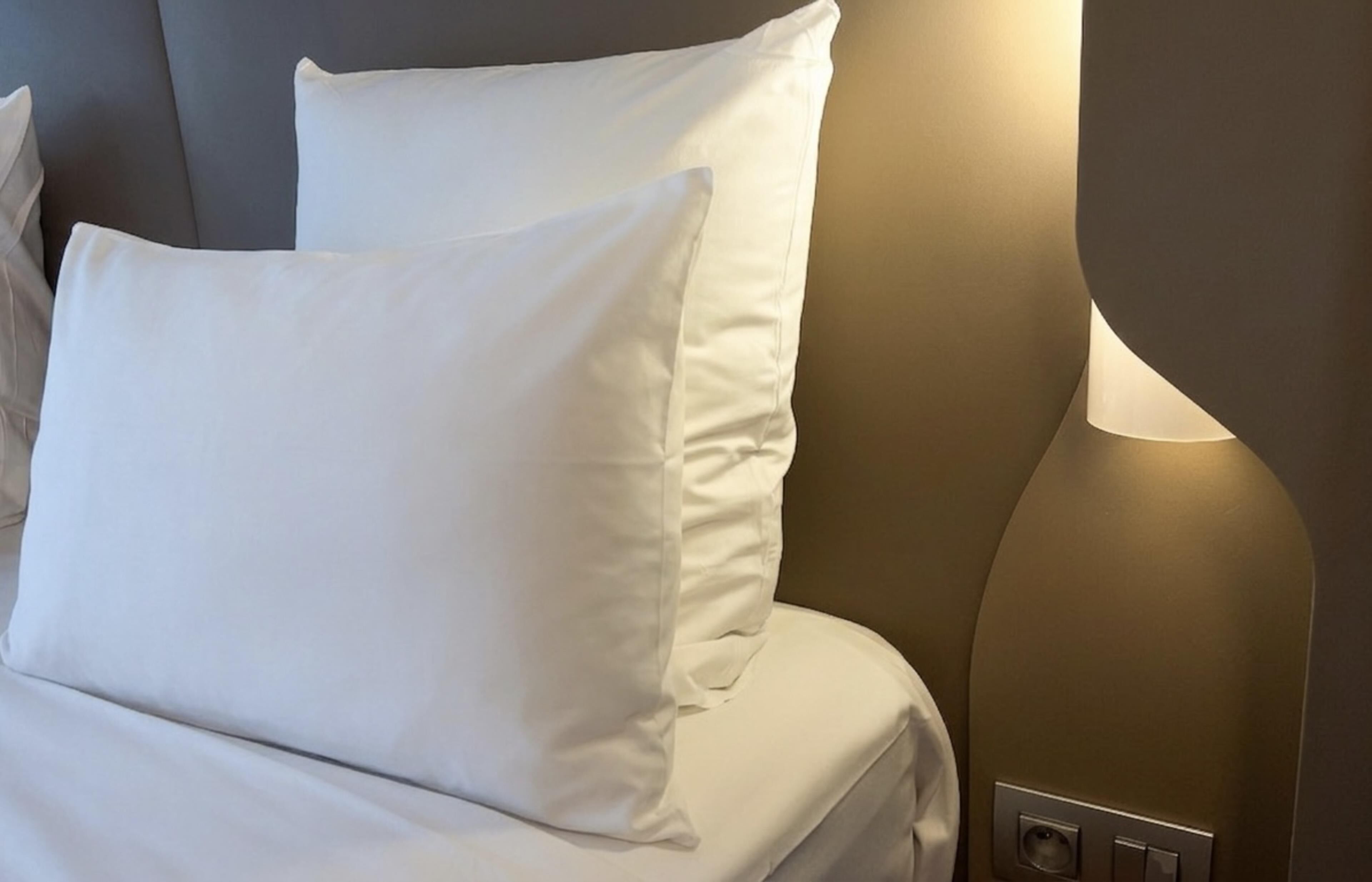 Ein Bett mit weißer Bettwäsche und einer Wandleuchte.