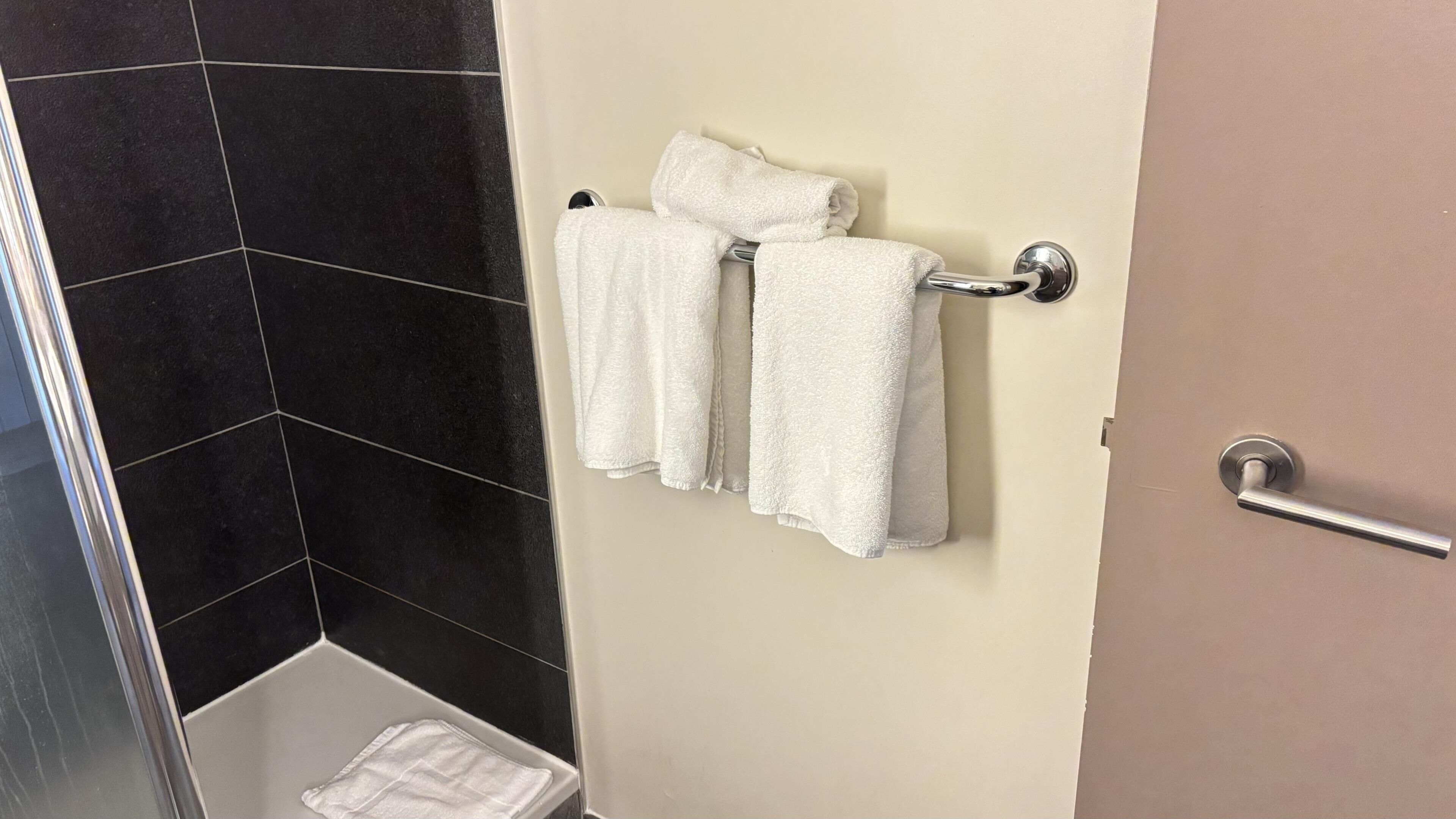 A bathroom with black tiled walls, a white towel rack with two towels, and a shower area.